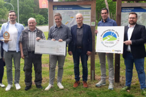 Landrat Markus Ramers (3.v.l) und Bürgermeister Dr. Hans-Peter Schick (4.v.l.) übergaben einen Sieger-Award, eine Wanderbank sowie eine Geldprämie in Höhe von 300 Euro für die Vereinskasse an den „Vater“ der EifelSpur Horst Müller (2.v.l). Bild: Dominik Ketz